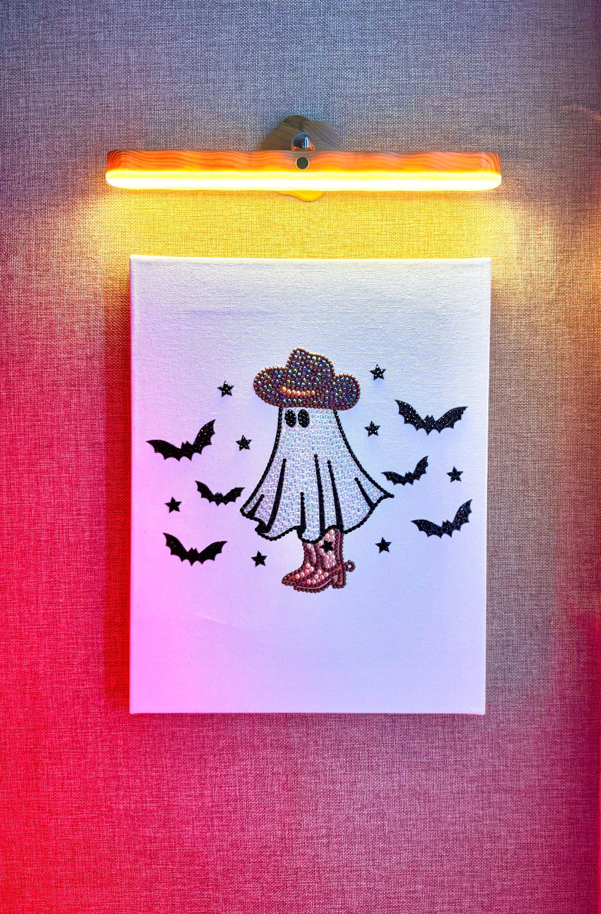 Rhinestone-bedazzled canvas wall art of a cartoon spooky ghost in a cowboy hat with ghosts flying around it.