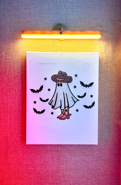 Rhinestone-bedazzled canvas wall art of a cartoon spooky ghost in a cowboy hat with ghosts flying around it.