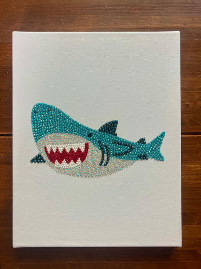 Hand-bedazzled canvas wall art depicting a blue shark with a open mouth, created using rhinestones.