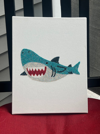 Hand-bedazzled canvas wall art depicting a blue shark with a open mouth, created using rhinestones.